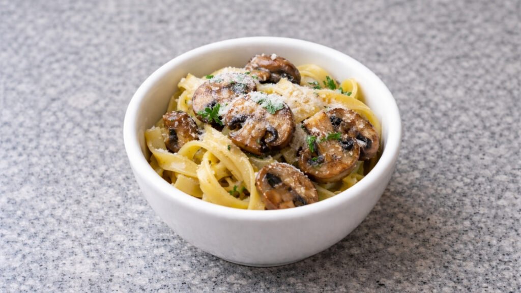 mushrooms and pasta in a white bowl on grey worktop